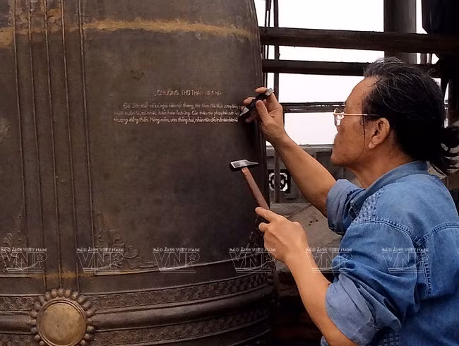 Nghệ nhân Nguyễn Văn Hiển đang miệt mài khắc chữ trên một chiếc chuông đồng lớn. (Nguồn: Trịnh Bộ/Báo ảnh Việt Nam)