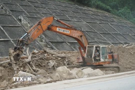 Đơn vị thi công phải dùng xe máy chuyên dụng để phá các tảng đá lớn nặng hàng chục tấn bị nước lũ cuốn lăn xuống đường. (Ảnh: Quốc Dũng/TTXVN)