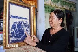 Nữ du kích Nguyễn Thị Thu bên bức ảnh “Cha con lão ngư dân Triệu Phong chở bộ đội và vũ khí tiếp sức Thành cổ” của phóng viên chiến trường Đoàn Công Tính (Báo Quân đội Nhân dân) ghi lại trên dòng Thạch Hãn vào mùa hè năm 1972. (Ảnh: Tường Vi/TTXVN)