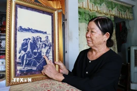 Nữ du kích Nguyễn Thị Thu bên bức ảnh “Cha con lão ngư dân Triệu Phong chở bộ đội và vũ khí tiếp sức Thành cổ” của phóng viên chiến trường Đoàn Công Tính (Báo Quân đội Nhân dân) ghi lại trên dòng Thạch Hãn vào mùa hè năm 1972. (Ảnh: Tường Vi/TTXVN)
