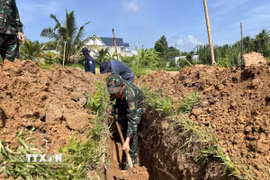 Các lực lượng khẩn trương tìm kiếm hài cốt liệt sỹ tại nghĩa trang liệt sỹ tạm ấp Tân Hòa. (Ảnh: Huỳnh Phúc Hậu/TTXVN)