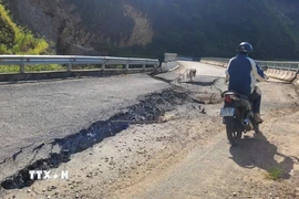 Người dân di chuyển qua những điểm nứt gãy của mặt cầu. (Ảnh: Nguyễn Oanh/TTXVN)
