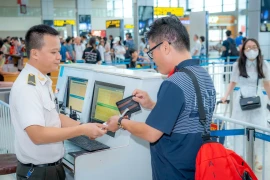 Nhân viên an ninh hàng không kiểm tra giấy tờ hành khách làm thủ tục lên máy bay. (Ảnh: PV/Vietnam+)