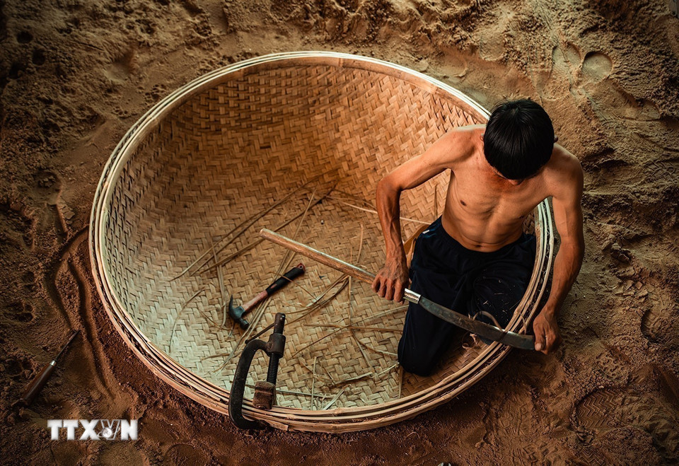 Người thợ đào hầm đất làm khuôn rồi đặt nguyên tấm mê thúng đã đan xong xuống hầm. Công đoạn lận vành là một trong những công đoạn quan trọng quyết định đến chất lượng sản phẩm để chiếc thúng sau khi lận cả vòng thúng và vành phải tròn đều, cân bằng và không biến dạng.” (Ảnh: Khánh Hòa/TTXVN)