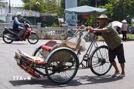 Nhọc nhằn đẩy xe xích lô lên dốc giữa nắng nóng gay gắt ở gần cầu Gia Hội, phường Phú Xuân, thành phố Huế. (Ảnh: Nguyên Lý/TTXVN)