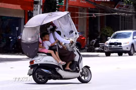 Giữa đỉnh điểm nắng nóng mùa hè, nhiều người dân lắp thêm mái che chống nắng cho xe máy khi chở trẻ nhỏ di chuyển trên đường phố tỉnh Phú Thọ. (Ảnh: Hoàng Hùng/TTXVN)