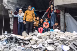 Người dân Palestine đứng trên đống đổ nát của những tòa nhà bị phá hủy sau các cuộc không kích của Israel xuống Dải Gaza. (Ảnh: THX/TTXVN)