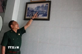 Cựu chiến binh Trần Dân bên bức hình chụp cùng đồng đội tại Dinh Độc Lập vào 13h30 ngày 30/4/1975. (Ảnh: Hoàng Ngà/TTXVN)