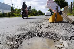 Người dân đặt vật dụng cảnh báo người lái xe né tránh các ổ gà, ổ voi trên quốc lộ 80. (Ảnh: Văn Sĩ/TTXVN)