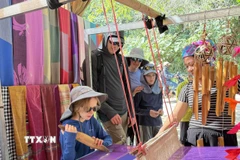 Du khách quốc tế thích thú khi được trải nghiệm quá trình dệt thổ cẩm của người dân tộc Thái. (Ảnh: Hoa Mai/TTXVN)