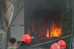 Lực lượng chức năng huy động xe cần cẩu phá mặt tiền bằng tôn của cửa hàng để phun nước vào trong. (Ảnh: Quốc Dũng/TTXVN)