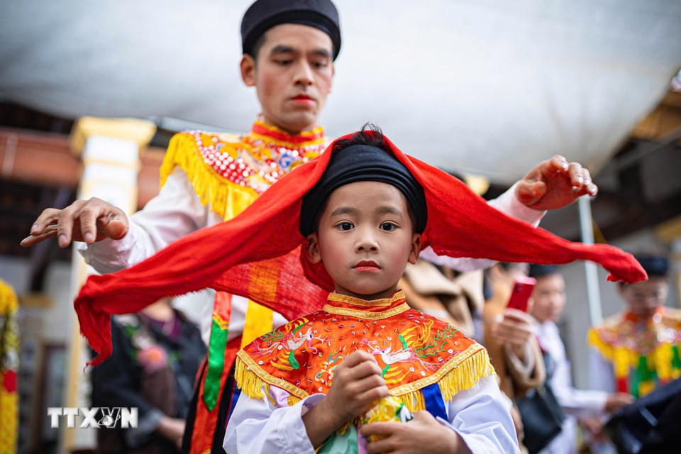 Thành viên CLB trống bồng Triều Khúc hỗ trợ chít khăn mỏ quạ cho em nhỏ. (Ảnh: Phạm Tuấn Anh/TTXVN)
