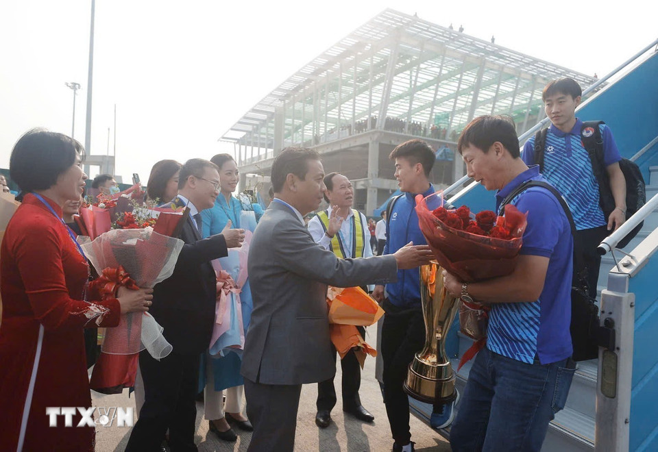 Thứ trưởng Bộ Văn hóa, Thể thao và Du lịch Hoàng Đạo Cương và Phó Cục trưởng Cục TThể dục Thể thao Lê Thị Hoàng Yến đón, tặng hoa chúc mừng Huấn luyện viên Kim Sang-sik và đội tuyển tại chân cầu thang máy bay. (Ảnh: Minh Quyết/TTXVN)