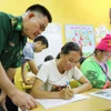 Thiếu tá Lò Thanh Chuyển, Đồn Biên phòng Leng Su Sìn, đến lớp học xóa mù chữ tại bản Cà Nà Pá để hỗ trợ giáo viên và các học viên tại đây. (Ảnh: Trung Kiên/TTXVN)