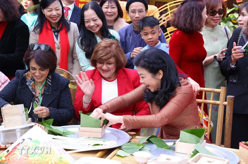 Bà Ngô Phương Ly, Phu nhân Tổng Bí thư Tô Lâm với các đại biểu trải nghiệm gói và luộc bánh chưng. (Ảnh: Văn Điệp/TTXVN)