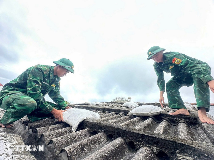 Các chiến sỹ giúp người dân đưa bao cát lên mái nhà để tránh tốc mái tôn khi gió bão. (Ảnh: TTXVN phát)