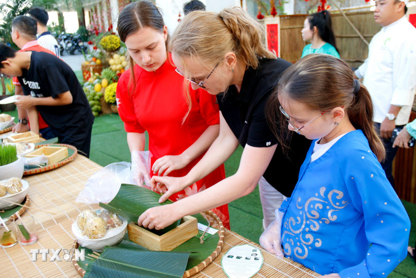 Du khách quốc tế trải nghiệm tập gói bánh chưng lá dong. (Ảnh: Nguyễn Thanh/TTXVN)