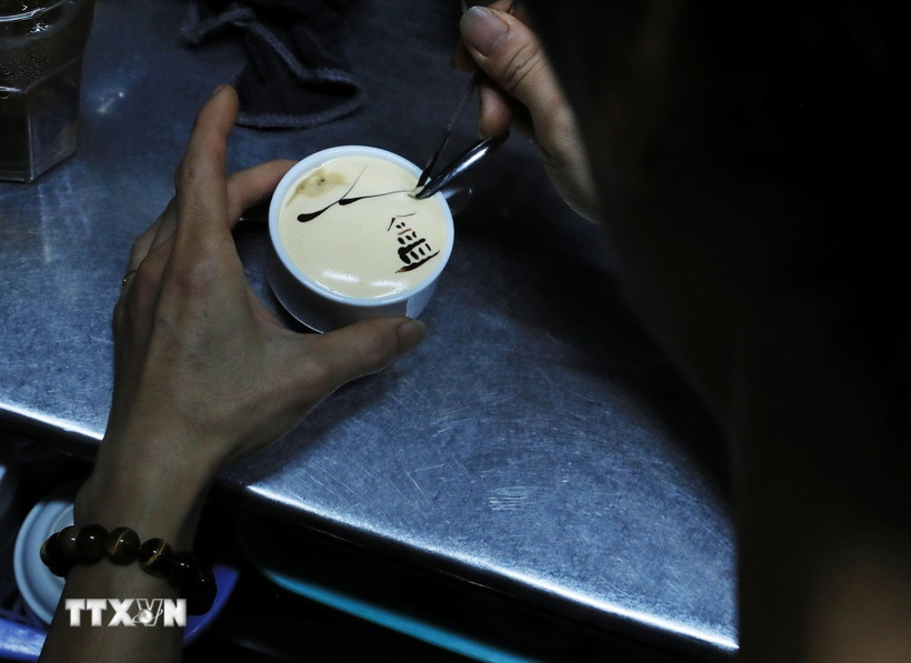 អ្នកក្រឡុកស្រាតុបតែងពែងកាហ្វេស៊ុតជាមួយនឹងរូបភាពនៃអគារអណ្តើក។ (រូបថត៖ Lam Khanh/VNA)