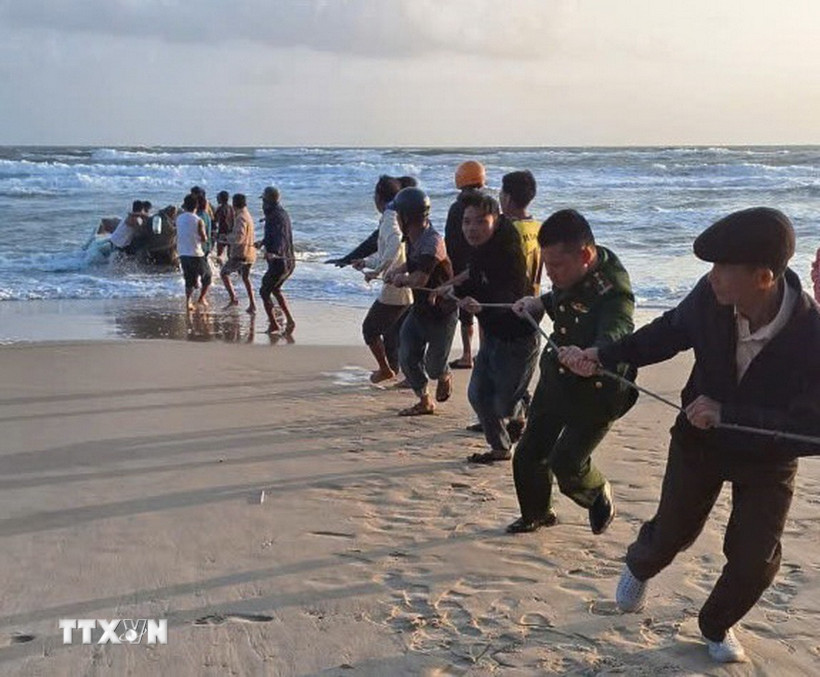 Các lực lượng chức năng và người dân triển khai kéo ghe vào bờ. (Ảnh: TTXVN phát)