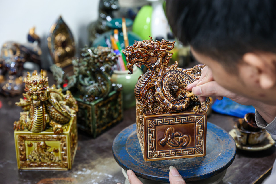 Anh Mạc Triều Dương, một thợ thủ công cho biết mỗi sản phẩm rồng sẽ được vẽ hoàn thiện trong khoảng 2 tiếng rưỡi. Mỗi ngày một thợ thủ công có thể hoàn thiện được 5-6 sản phẩm. Người thợ sẽ dùng dung dịch vẽ vàng 24K để trang trí cho sản phẩm sau đó sẽ được mang đi nung lần 2 ở nhiệt độ phù hợp trong khoảng 6-8 tiếng để tạo nên lớp mạ vàng sang trọng. (Ảnh: Minh Sơn/Vietnam+)