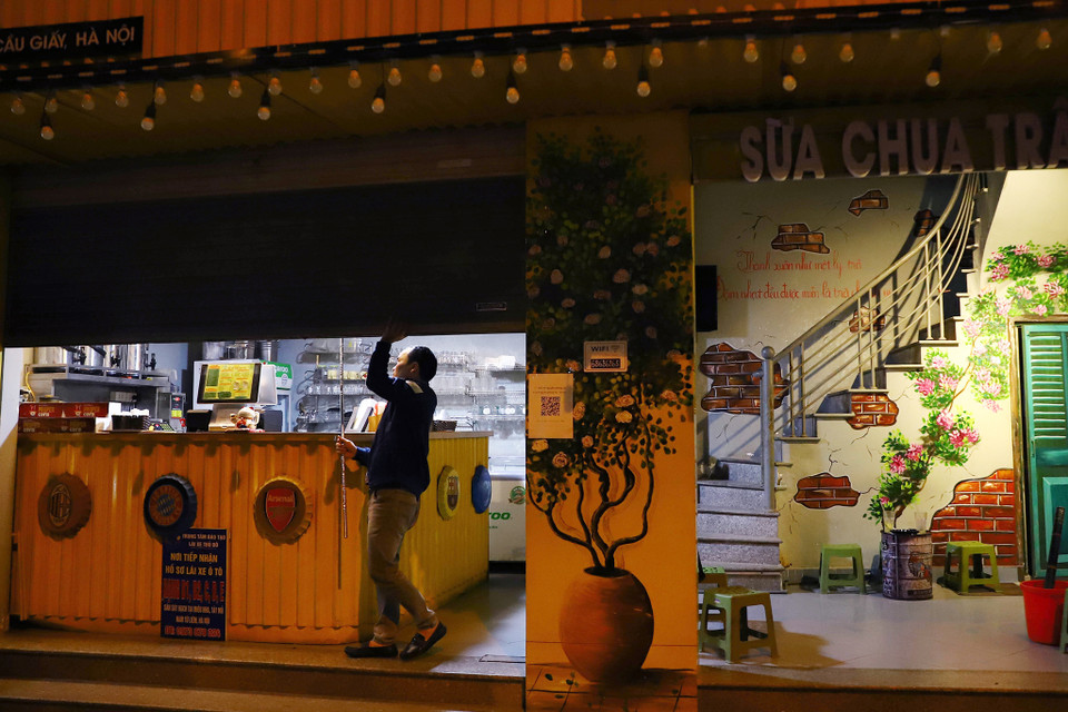 Tình hình dịch COVID-19 hiện nay có nhiều chuyển biến phức tạp. Do đó, người dân cần có ý thức chung tay chấp hành đúng quy định để đẩy lùi dịch bệnh. Anh Tâm- chủ tiệm trà chanh tại 97b Nguyễn Phong Sắc chia sẻ:’ Tôi luôn giục khách ra về từ trước 21h và từ chối nhận khách để đóng cửa. Có những hôm khách phật ý bỏ về nhưng tôi phải đảm bảo thực hiện đúng quy định đã đề ra.’ Lực lượng chức năng cũng cần làm chặt chẽ hơn trong việc nhắc nhở cũng như xử lí các cửa hàng vi phạm. (Ảnh: Hoài Nam/Vietnam+)