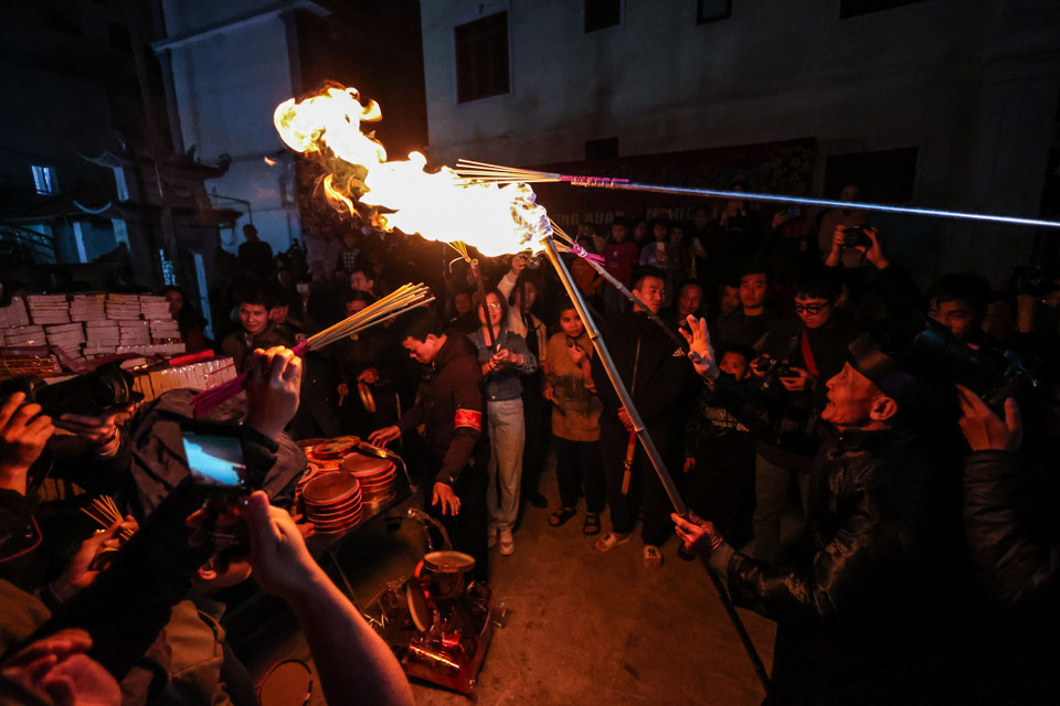 Đúng 21 giờ, cụ từ vào trong hậu cung lấy lửa ra chuẩn bị 'tán lộc 'cho dân làng. Cụ từ châm lửa từ trong đình bằng một cây gậy dài rồi mang ra sân. (Ảnh: Minh Sơn/Vietnam+)