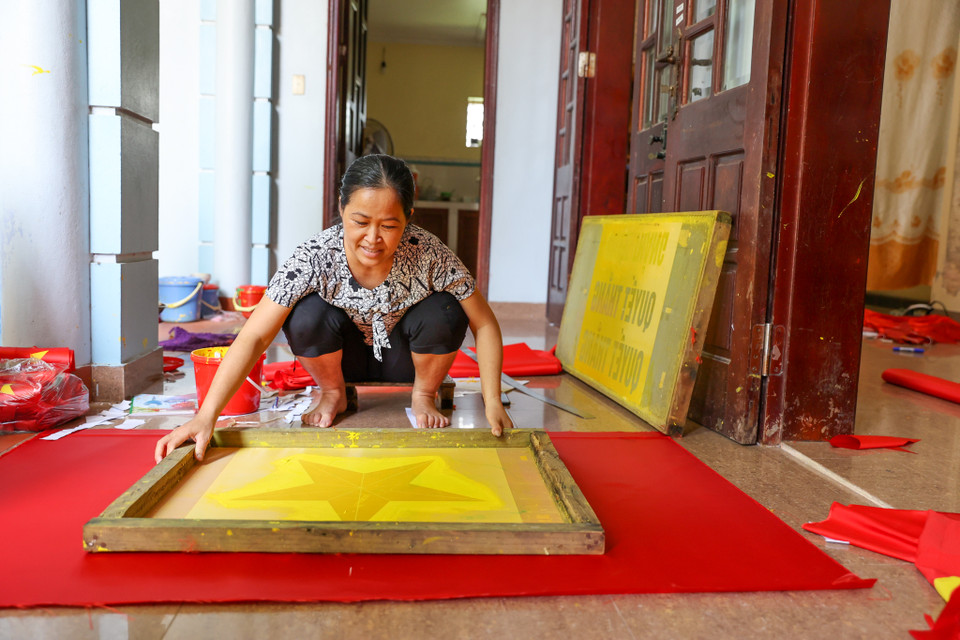 Chị Nhung năm nay 46 tuổi nhưng đã có hơn 30 năm chuyên thêu cờ Tổ quốc. Chị cho biết nhà chị đã có truyền thống may cờ 3 đời tại làng. Bố chị những năm trước phải học nghề may cờ rồi mới về truyền cho con cháu. Hơn chục năm trở lại đây, nhu cầu về cờ Tổ quốc tăng mạnh, gia đình chị trở nên tất bật hơn. (Ảnh: Minh Sơn/Vietnam+)