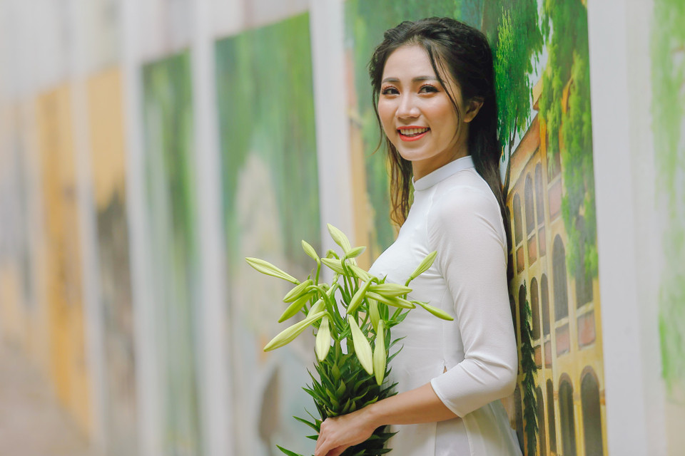 Giữa phố phường tấp nập, chợt thấy màu trắng trong của hoa loa kèn nghe thân thương đến lạ. Hình ảnh thiếu nữ và hoa loa kèn trong tay đi giữa những vạt nắng lung linh đang ùa về trên phố. (Ảnh: Thế Đại/Vietnam+)