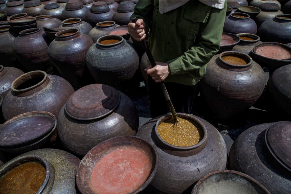 Hàng ngày người thợ phải mở nắp chum khuấy đều và cho thêm nước vào tương, trời nắng thì phơi, trời mưa thì phủ kín miệng để nước mưa không lọt vào tương nếu không tương sẽ bị ủng. (Ảnh: Thế Đại/Vietnam+)