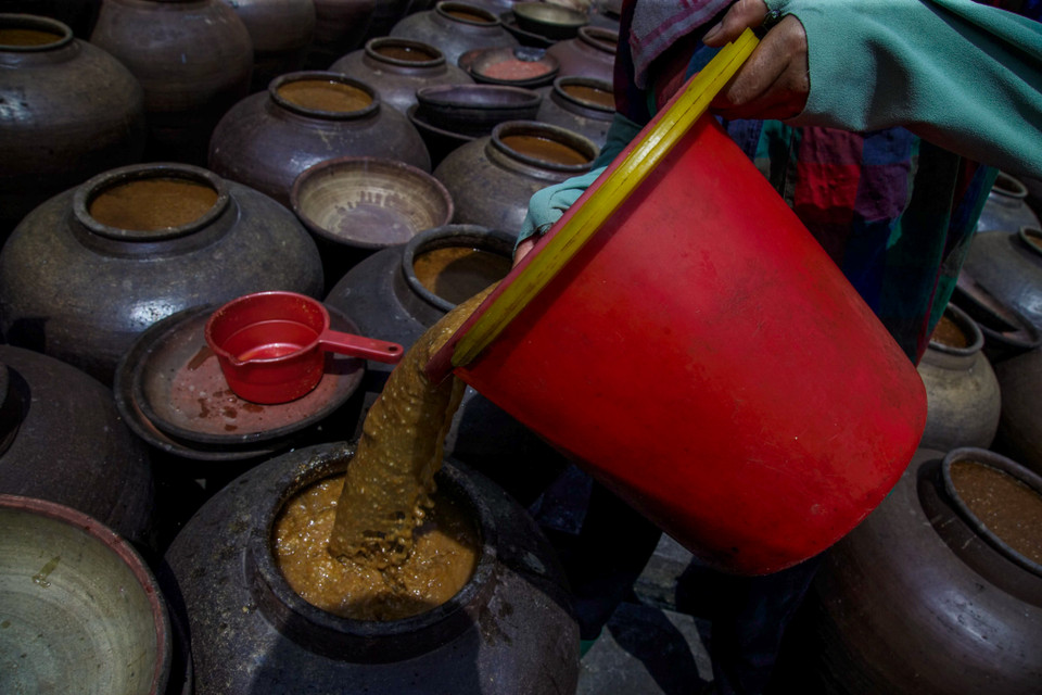 Tương được phơi nắng trong vòng ít nhất 1 tháng và luôn được theo dõi cẩn thận. Để tương nhuyễn và lên màu, người làm tương phải thường xuyên khuấy tương vào buổi sáng và trưa. Ánh sáng mặt trời làm nóng chum giúp tương chín nhanh hơn. Trời càng nhiều nắng thì tương chín càng nhanh(Ảnh: Thế Đại/Vietnam+)