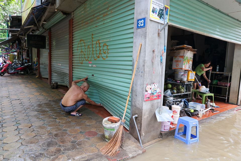 Một hộ gia đình đang cố gắng sửa lại những chiếc cửa cuốn bị sóng từ các phương tiện di chuyển nhanh đánh móp khi nước dâng cao. (Ảnh: Minh Sơn/Vietnam+)