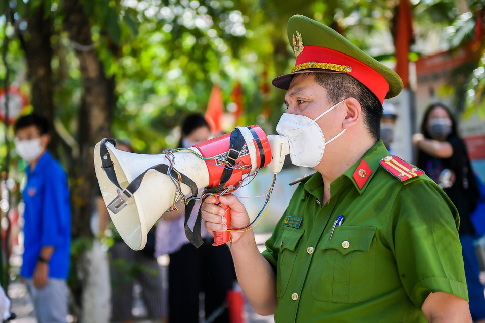 Công an phường liên tục nhắc nhở các phụ huynh học sinh không đứng chờ con em mình trước điểm thi, đảm bảo giữ khoảng cách an toàn. (Ảnh: PV/Vietnam+)