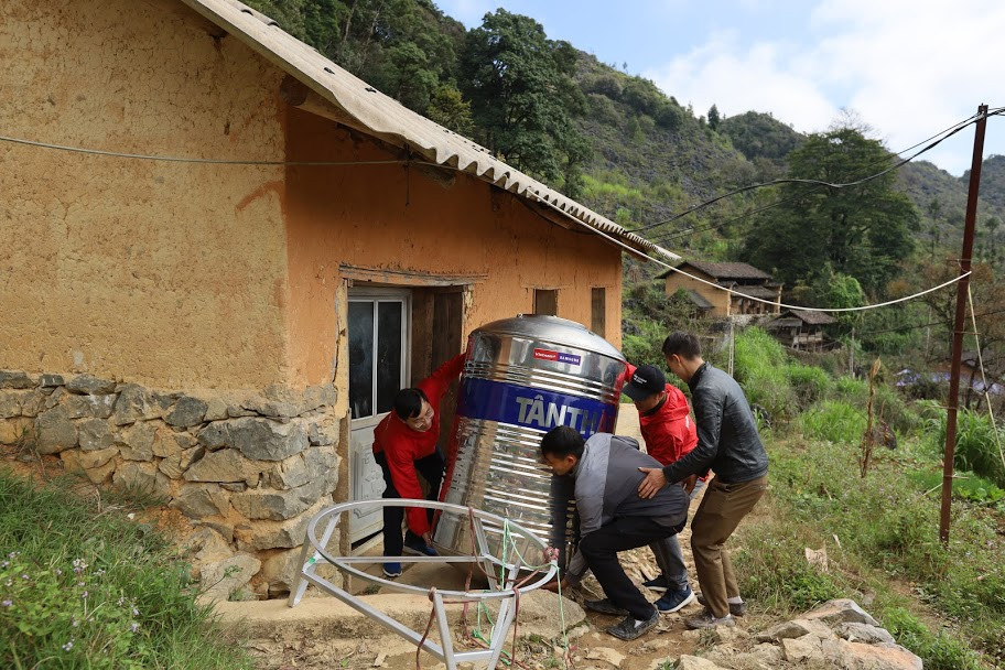 Ông Trần Tiến Duẩn - Tổng Biên tập Báo Điện tử VietnamPlus và ông Nguyễn Hoàng Nhật - Phó Tổng Biên tập Báo Điện tử VietnamPlus (áo đỏ) đang cùng bà con tại Lủng Sính bê bồn chứa nước về nhà. (Ảnh: Minh Sơn/Vietnam+)