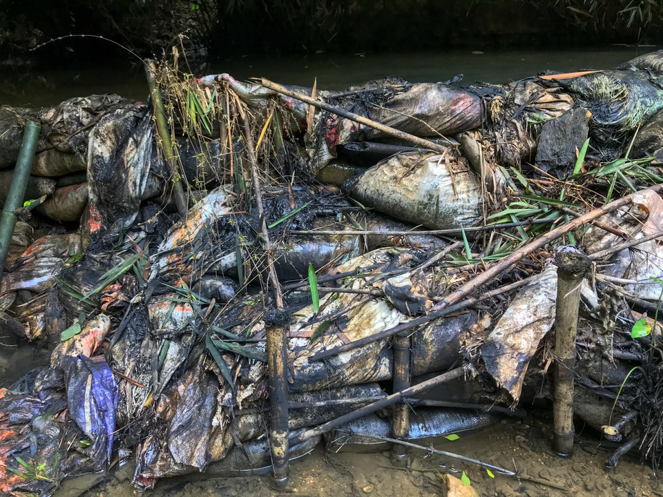 Tuy nhiên, chiếc kè thô sơ này cũng không ngăn cản được bao nhiêu. Dầu thải vẫn cuồn cuộn theo dòng nước đổ về hạ nguồn. (Ảnh: PV/Vietnam+)