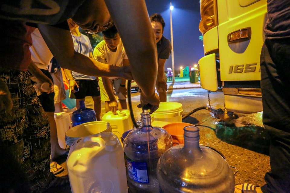 Người dân kiên nhẫn chờ nước sạch được bơm đầy bình, đầy xô chậu trước khi đưa lên nhà. (Ảnh: Minh Sơn/Vietnam+)