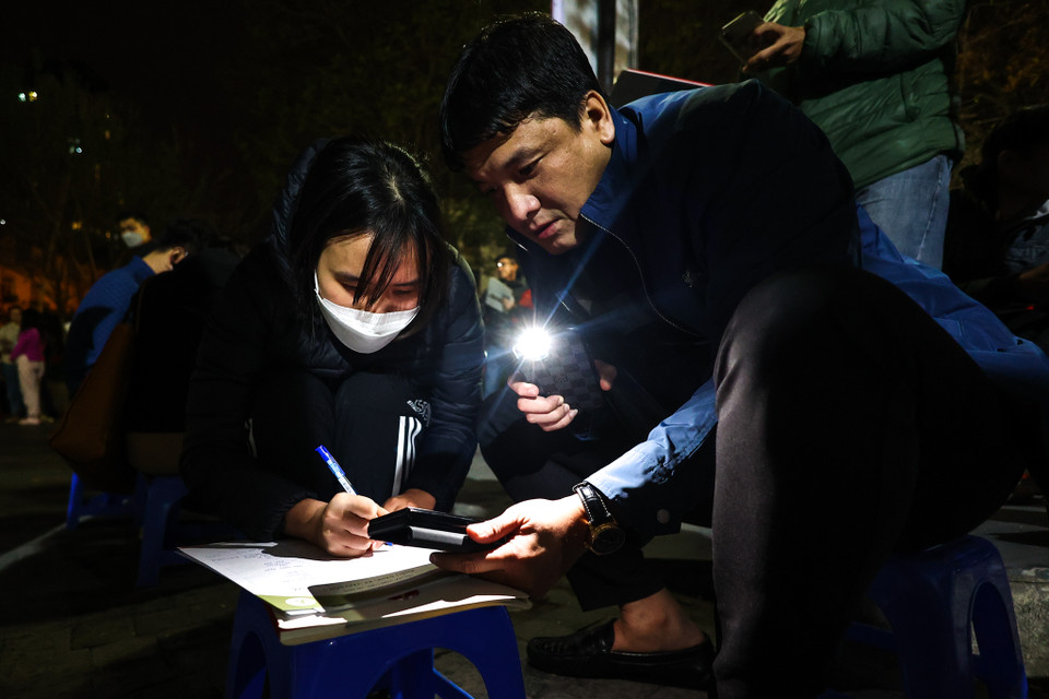 Nhiều phụ huynh bật đèn flash, kê khai thông tin đăng ký ở ngoài cổng trường do không đủ chỗ ngồi ở khu vực bàn đăng ký. (Ảnh: Minh Sơn/Vietnam+)