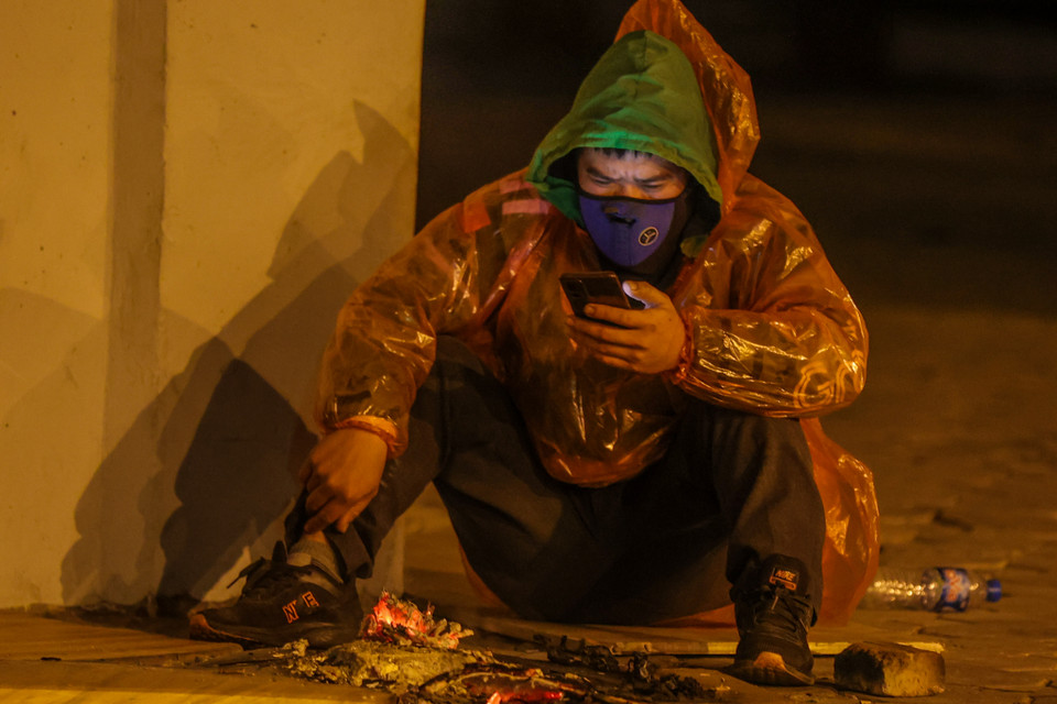 Một tài xế xe ôm công nghệ trong lúc chờ khách phải đốt lửa sưởi ấm và mặc thêm áo mưa để chống chọi nhiệt độ càng lúc càng lạnh. (Ảnh: Minh Sơn/Vietnam+)