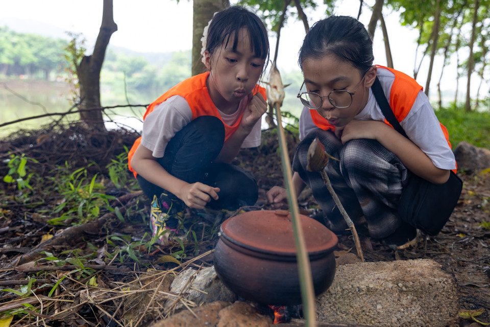 Hai bạn nhỏ B.M (12 tuổi trường Xuân La, Tây Hồ) và B.N (11 tuổi, trường Thanh Xuân Trung) tỏ ra hào hứng cho biết đây là lần đầu tiên các em được trải nghiệm việc kiếm củi, tạo ra lửa để nấu cơm, nướng thịt. (Ảnh: Minh Sơn/Vietnam+)