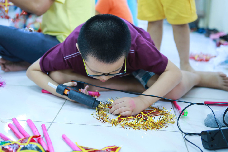 Một cậu bé chăm chú bắn keo vào chiếc lồng đèn ông sao. (Ảnh: Minh Sơn/Vietnam+)