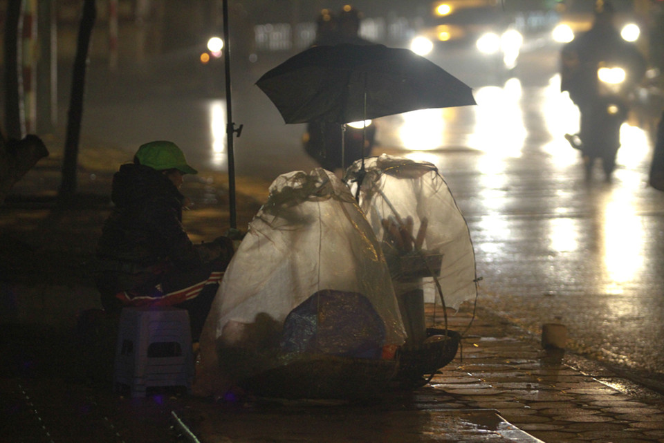 Giữa thành phố ồn ã, người lao động nghèo vẫn cố gắng bươn chải dù thời tiết không ủng hộ. (Ảnh: Minh Sơn/Vietnam+)