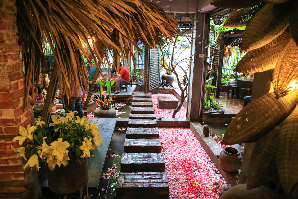 Anh Nguyên, chủ quán chia sẻ: ‘Mỗi ngày mình đều bỏ rất nhiều công sức ra để phủ đầy cánh hoa trên cái ao nhỏ kết hợp với những bộ bàn ghế tre, những vật dụng trang trí nho nhỏ sẽ khiến mọi người đến đây nhớ về một vùng quên thanh bình, yên ả. Khách vừa đến ăn vừa được thư giãn mới là mục đích của mình’. (Ảnh: Trung Kiên/Vietnam+)