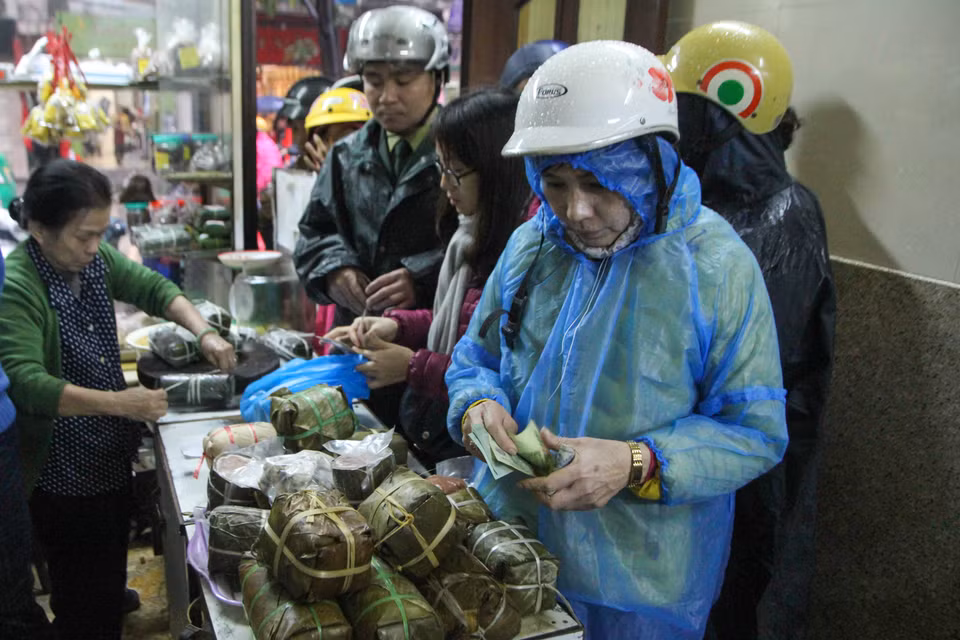 Thậm chí ngay cả khi trời mưa to, có người vẫn chấp nhận mặc áo mưa để mua được một cặp bánh chưng, một khoanh giò lụa. (Ảnh: Minh Sơn/Vietnam+)