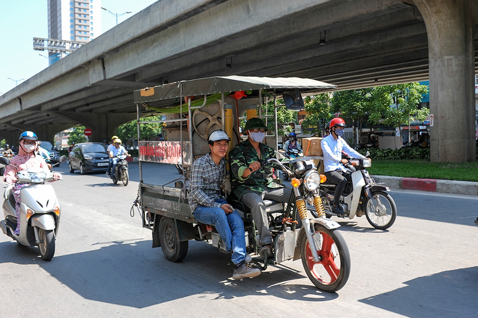 Khoảng 12 giờ trưa, cái nóng hầm hập bốc lên từ mặt đường giữa kết hợp với làn khói xe nóng bỏng rát mặt, những người lao động vẫn phải vắt kiệt sức mình trên từng mét đường để mưu sinh. (Ảnh: Minh Sơn/Vietnam+)