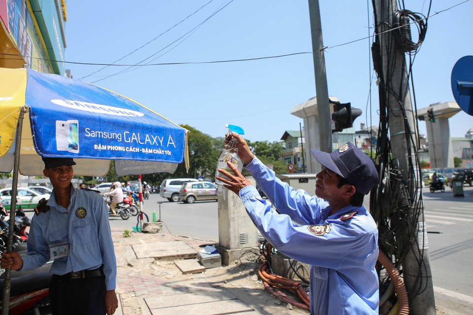 Bác bảo vệ già phải dùng bình xịt nước lên ô che cho bớt nóng nhưng đây cũng chỉ là giải pháp tạm thời vì nước cũng bay hơi trong ít phút. (Ảnh: Minh Sơn/Vietnam+)