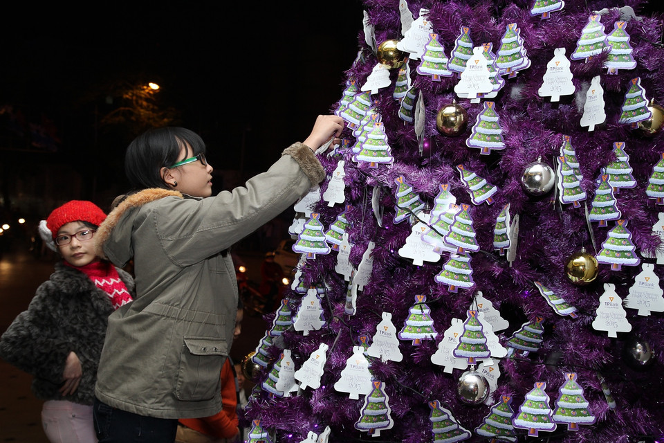 Bé gái đang treo thiệp điều ước lên cây thông tím. (Ảnh: PV/Vietnam+)