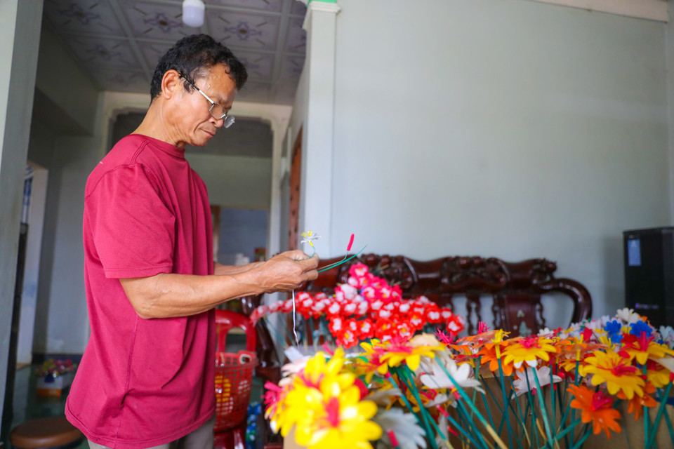 Ông Nguyễn Hóa có hơn 40 năm làm nghề hoa giấy cho biết, dịp cận Tết ông và gia đình cần làm trên dưới 2.000 cặp hoa thờ cúng để cung cấp ra thị trường. Những lúc cao điểm không có người làm, các gia đình làm hoa ở Thanh Tiên phải nhờ hàng xóm sang làm giúp cho kịp hoa để bán. (Ảnh: PV/Vietnam+)