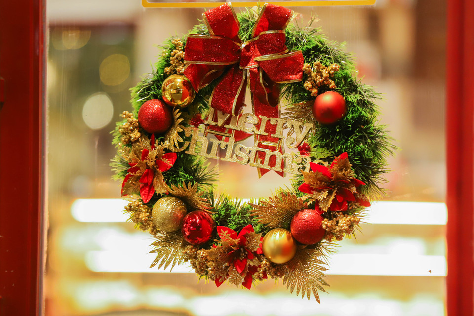 Ngoài những hộp quà, vòng nguyệt quế đính quả châu và dòng chữ ‘Mery Christmas’ được tô điểm thêm bởi dây ruy băng đỏ cũng là món đồ trang trí được ưa chuộng.(Ảnh: Hoài Nam/Vietnam+)