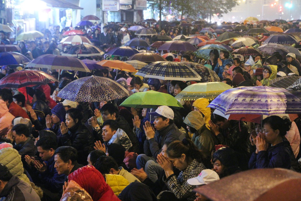 Thời tiết càng về tối mưa phùn càng nhiều nhưng người dân vẫn chấp nhận che ô để làm lễ cúng. (Ảnh: Minh Sơn/Vietnam+)