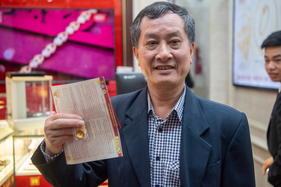 Ông Tô Hòa Bình, khách hàng đầu tiên tại Bảo Tín Minh Châu hào hứng chia sẻ 2 chỉ vàng mình mới mua được. Ông Bình cho biết đã mười mấy năm nay, ông luôn xếp hàng mua vàng tại đây từ 3 giờ sáng để lấy may. (Ảnh: Minh Sơn/Vietnam+)