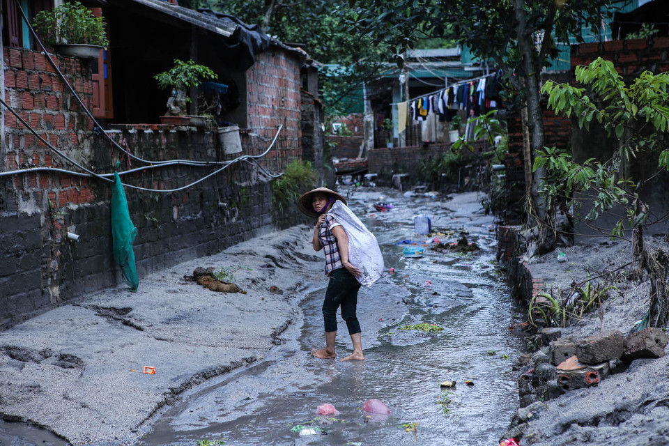 Theo con mương ngập đầy bùn lầy dẫn vào khu dân cư, khá đông người dân đang mang theo đồ đạc lội ngược ra. Người bê chăn màn, người ôm tivi, tủ lạnh mang ra nơi trú ẩn. (Ảnh: PV/Vietnam+)